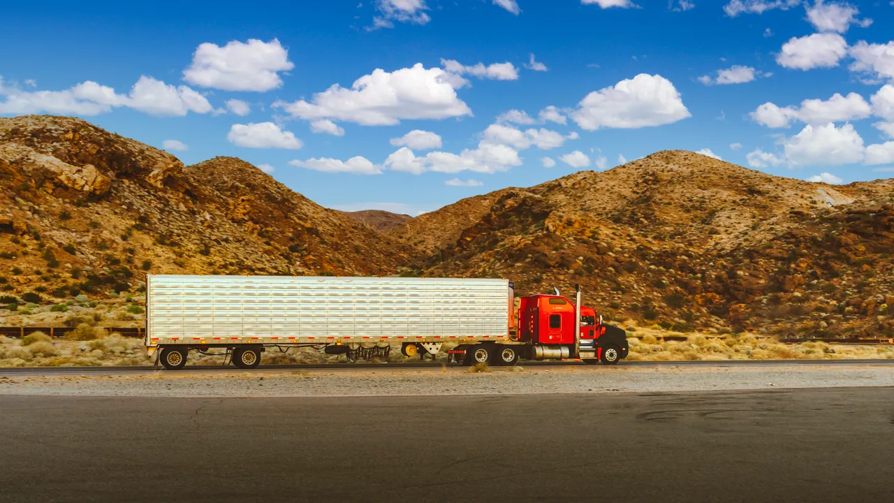 A red semi truck pulling a silver refrigerated trailer along a desert highway